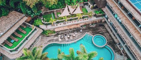 An aerial view of a resort with a central swimming pool, multiple lounge areas, and lush greenery.