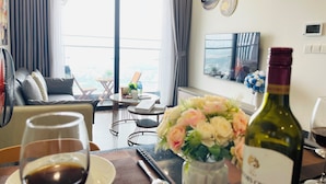 Un salon moderne avec un canapé, une table à manger agrémentée de verres à vin, un vase de fleurs et une bouteille de vin.