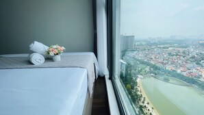 Une chambre d’hôtel avec un lit, une petite table sur laquelle est posé un vase de fleurs, et une vue sur le paysage urbain et la rivière.