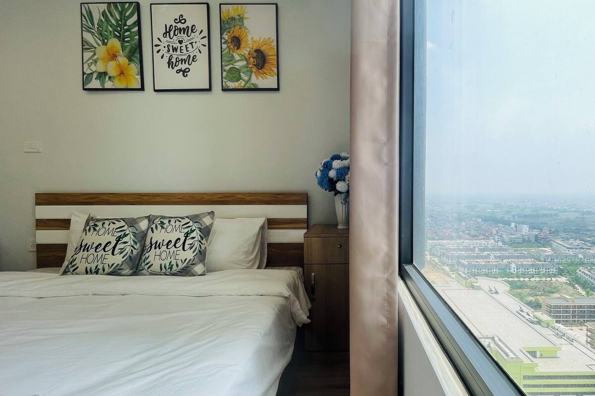 Un dormitorio con cama, almohadas y ventana con vista a la ciudad.