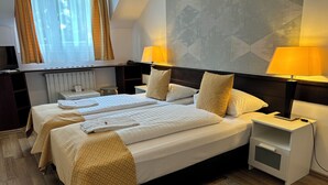 Een hotelkamer met twee bedden, een nachtkastje met lamp, een klein bureau en een radiator.