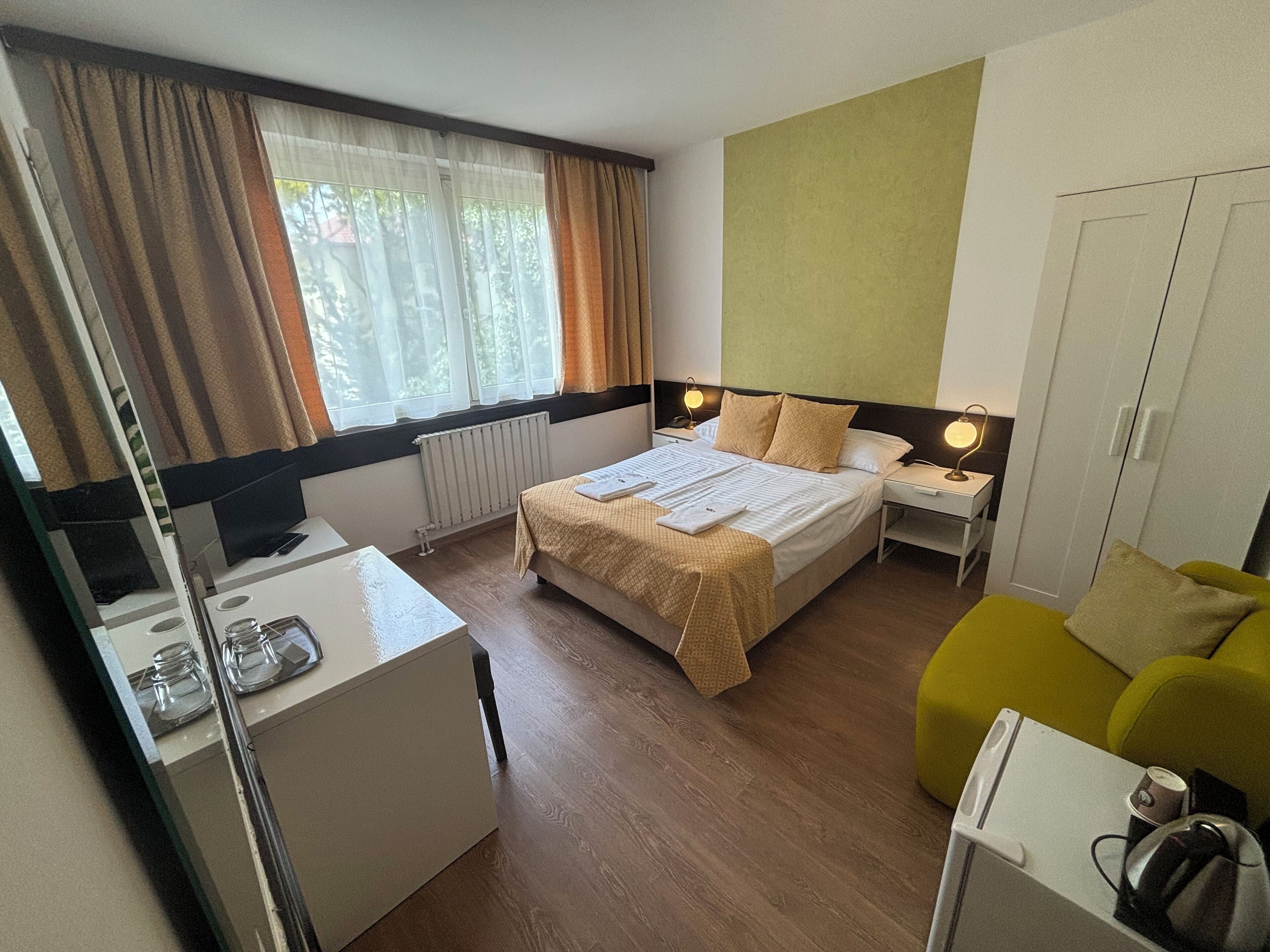 A hotel room with a bed, bedside tables, a desk, a chair, and a wardrobe.
