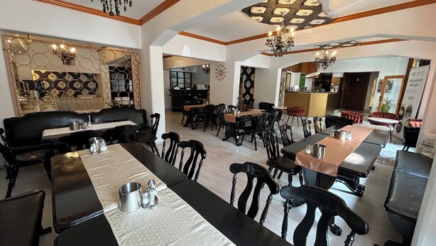 Een restaurant met verschillende eetgedeeltes, waaronder een lange gemeenschappelijke tafel en enkele kleinere tafels.