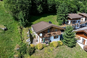 A wooden cabin with a balcony, surrounded by greenery and trees.