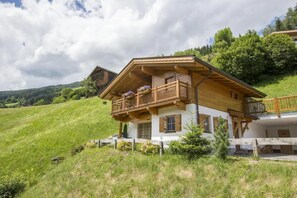 A two-story chalet with a balcony, surrounded by a grassy hillside. - Premium Mountain Chalet for 10 (Wald-Königsleiten)
