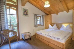 Quarto de madeira com cama, cadeira, janela e radiador.