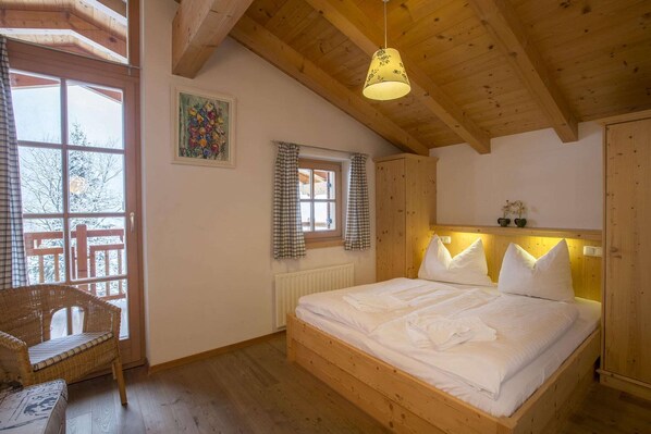 A wooden-framed bedroom with a bed, a window with curtains, a wicker chair, and a hanging light fixture. - Premium Mountain Chalet, Wald im Pinzgau (Wald-Königsleiten)