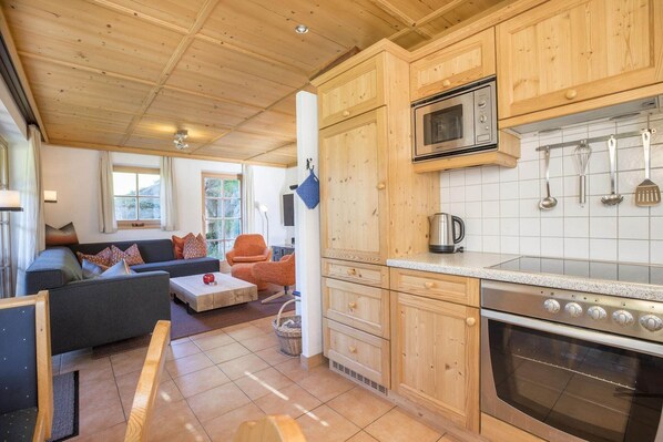 Cocina moderna con armarios de madera, microondas y horno. Cuenta con una zona de comedor con sofá y mesa de centro.