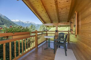 A wooden balcony with a table and chairs, overlooking a mountainous landscape.