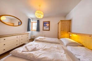 Une chambre à coucher avec un lit, une commode, un miroir, une fenêtre avec des rideaux et une affiche accrochée au mur.