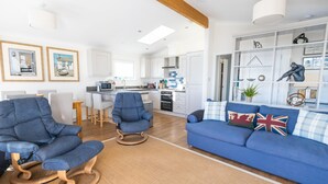 A modern living room with a blue sofa, two rocking chairs, and a dining area with a white table and chairs. - The Great Escape - a frontline lodge overlooking Avon Beach (Mudeford)