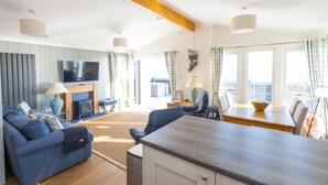 A modern living room with a sofa, dining table, and TV. - The Great Escape - a frontline lodge overlooking Avon Beach (Mudeford)