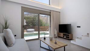 A modern living room with a large TV, a wooden coffee table, and a sofa. - Imbros Villas Free* Heated Pools in mountains! (Crete)