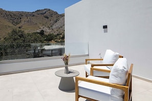 A balcony with a white wall, a wooden chair, a small round table, and a vase with flowers. - Imbros Villas Free* Heated Pools in mountains! (Crete)