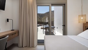 A bedroom with a bed, a desk, and a view of a patio with a table and chairs. - Imbros Villas Free* Heated Pools in mountains! (Crete)
