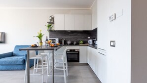 A modern kitchen with white cabinets, a black backsplash, and a dining area with white chairs.