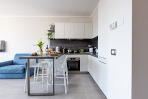 A modern kitchen with white cabinets, a black backsplash, and a dining area with white chairs.