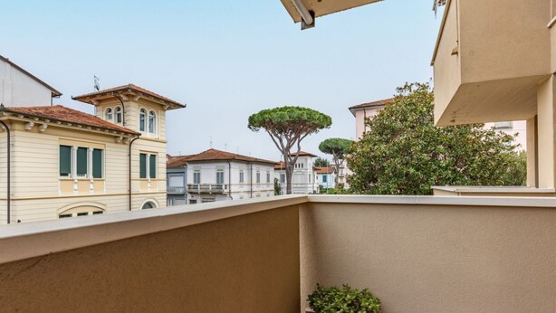 A balcony with a potted plant, a tiled floor, and a view of neighboring buildings.