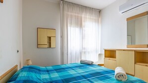 A bedroom with a bed, a bedside table, a lamp, a mirror, a wardrobe, and a window with curtains.