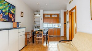 A compact kitchen with a dining area, a sofa, and a colorful artwork on the wall.