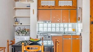 A compact kitchen with a stove, sink, and wooden cabinets. There is a dining table with chairs and a vase of flowers on the table.