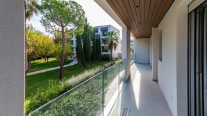 Un balcón con barandilla de vidrio que da a un jardín y un edificio moderno.