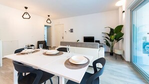 Un comedor moderno con una mesa blanca, sillas negras, lámparas colgantes hexagonales y un ventanal con vistas.