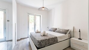 Un dormitorio moderno con cama, mesitas de noche, lámpara colgante y puerta corredera de vidrio.