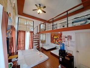 A compact hotel room with a bunk bed, a ceiling fan, a window with curtains, a wall with a coffee advertisement, and a welcome sign.