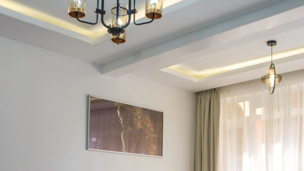 A hotel room with a large bed, a wooden headboard, a bedside table, a round table, a sofa, and a painting on the wall.
