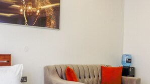 A hotel room with a bed, a sofa, a small table, a water dispenser, and a painting on the wall.