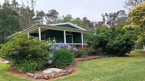 Une maison dotée d’un toit végétalisé, de murs extérieurs blancs et d’un porche abrité. Un jardin avec diverses plantes et fleurs se trouve devant la maison.