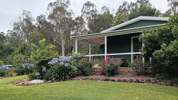 Une maison dotée d’un porche abrité, entourée d’un jardin bien entretenu où poussent diverses plantes et fleurs.