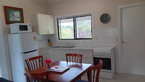 Une cuisine compacte avec des meubles blancs, un four à micro-ondes, un évier et une cuisinière. On y trouve une table à manger avec des chaises et une horloge au mur.