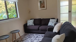 Un salon avec un canapé de couleur sombre, deux petites tables rondes, un tapis à motifs et un tableau encadré accroché au mur.