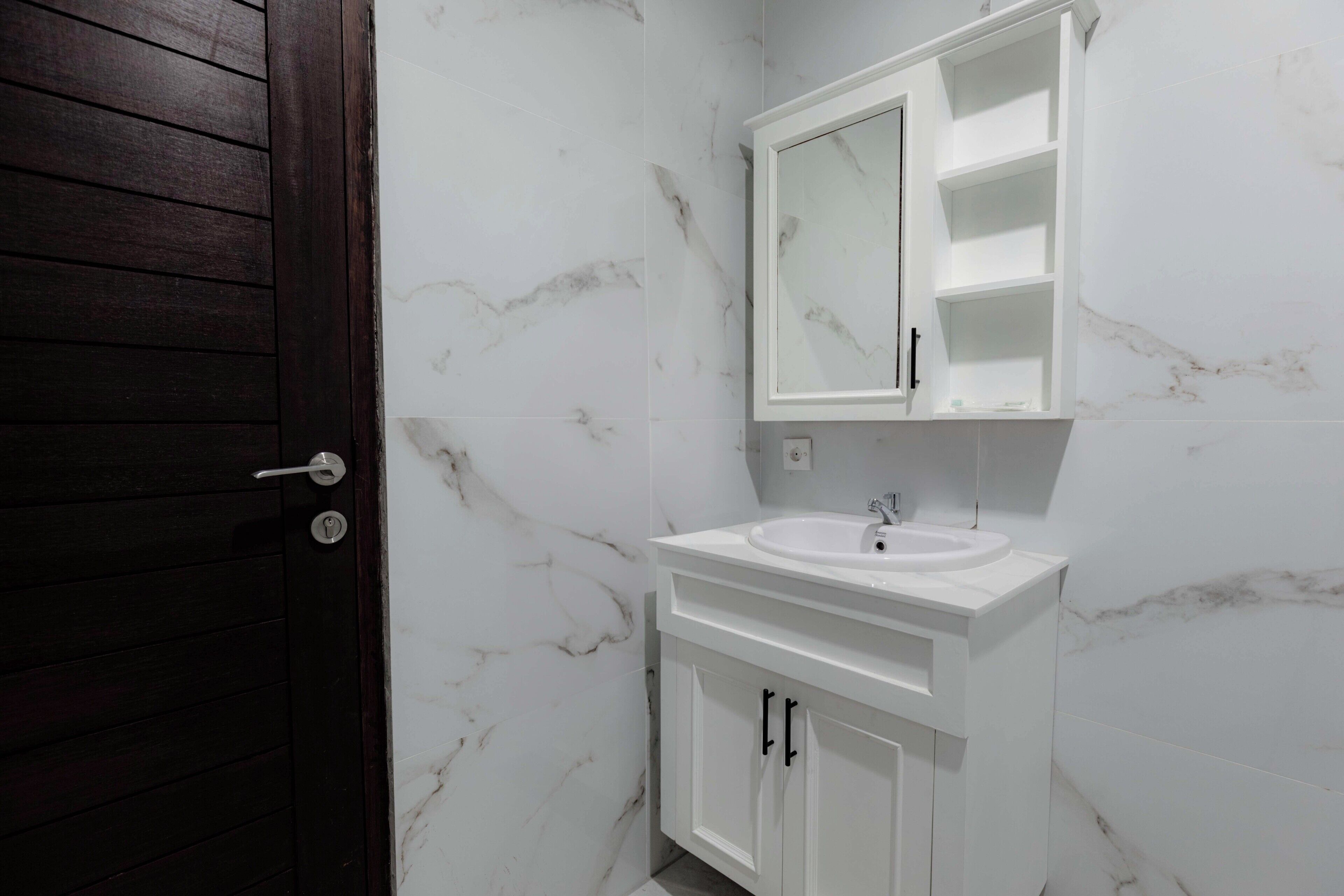 A bathroom with a white marble sink, a mirror above it, and white cabinets.