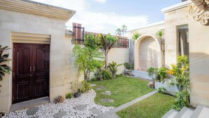 Un patio con un sendero de piedra, plantas en macetas y una puerta de madera grande.