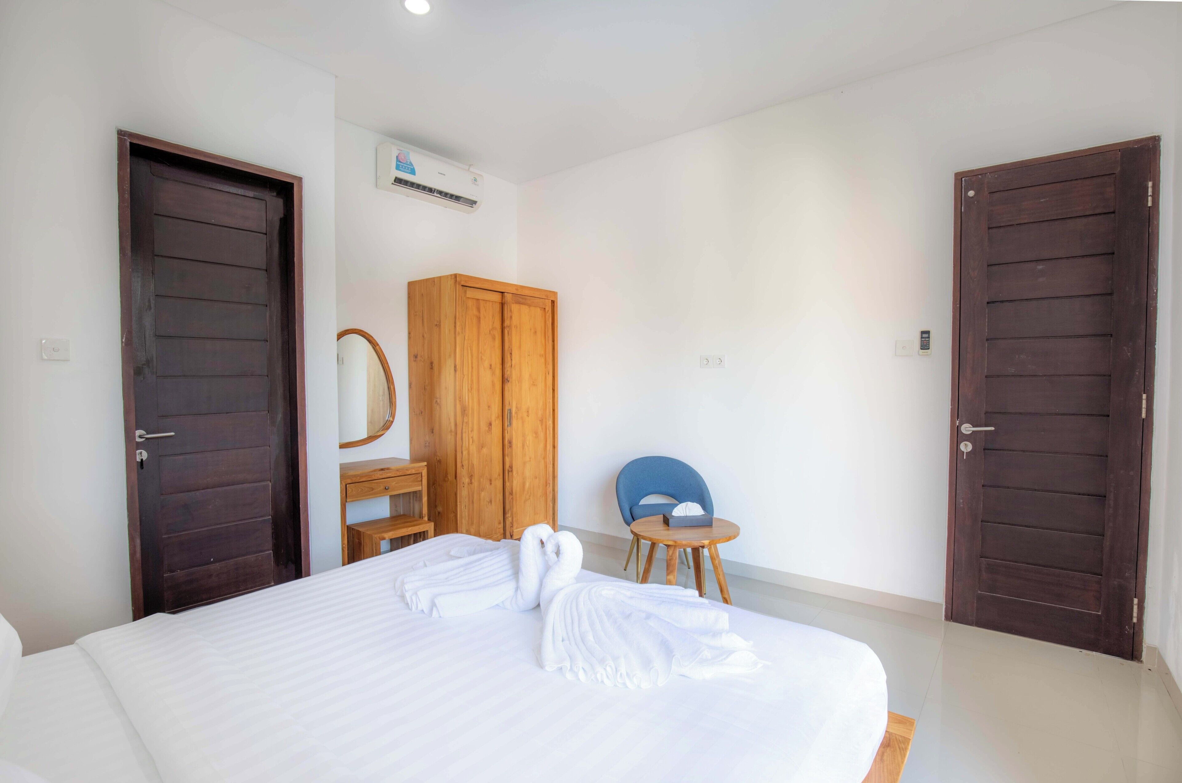A hotel room with a large bed, wooden wardrobe, a small desk with a chair, and a blue chair.