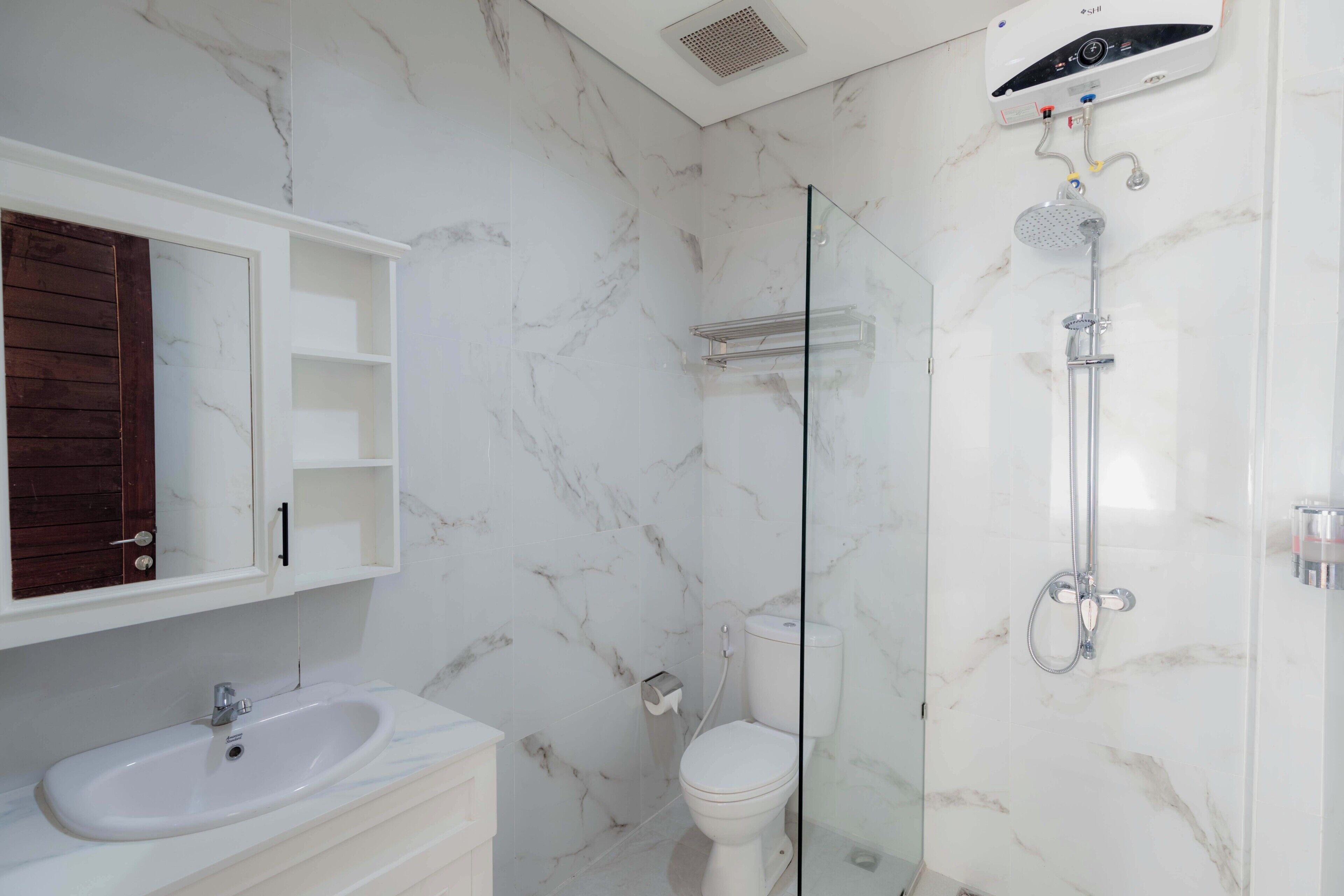 A bathroom with a marble wall, a glass shower enclosure, a white sink, and a toilet.