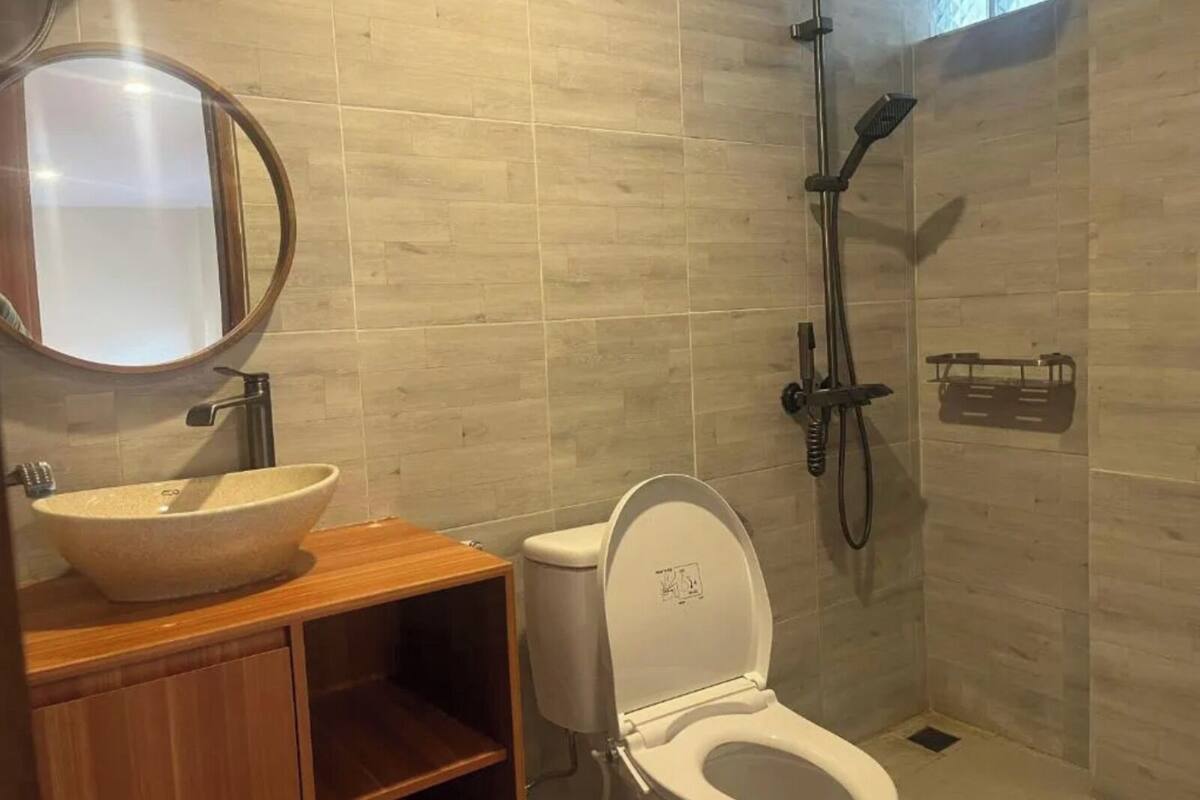 Ein Badezimmer mit einem Holzbidet, einem runden Spiegel, einer weißen Toilette und einer Dusche mit Duschbrause.
