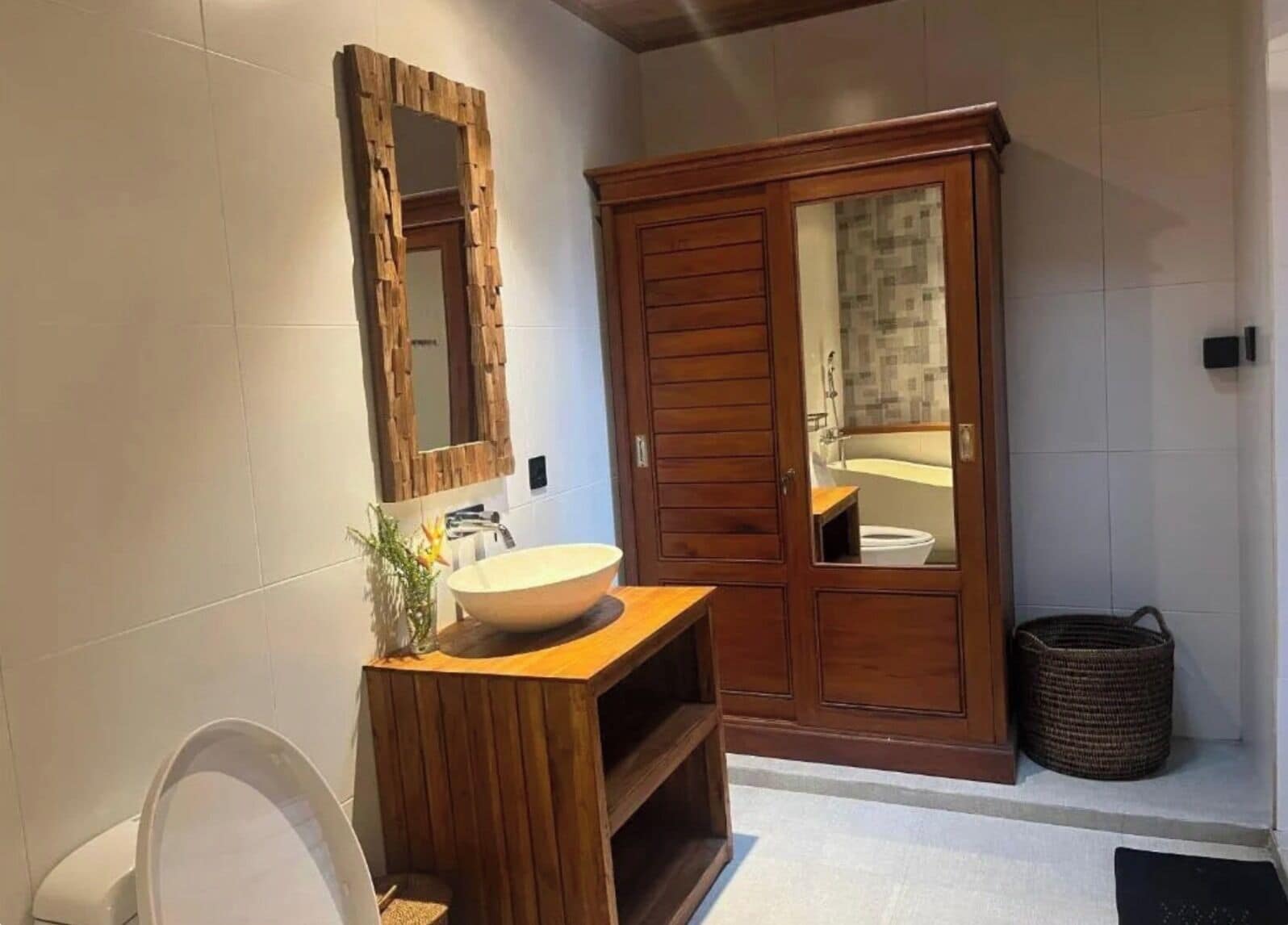 A bathroom with a wooden vanity, a large mirror, a white sink, and a wooden wardrobe.