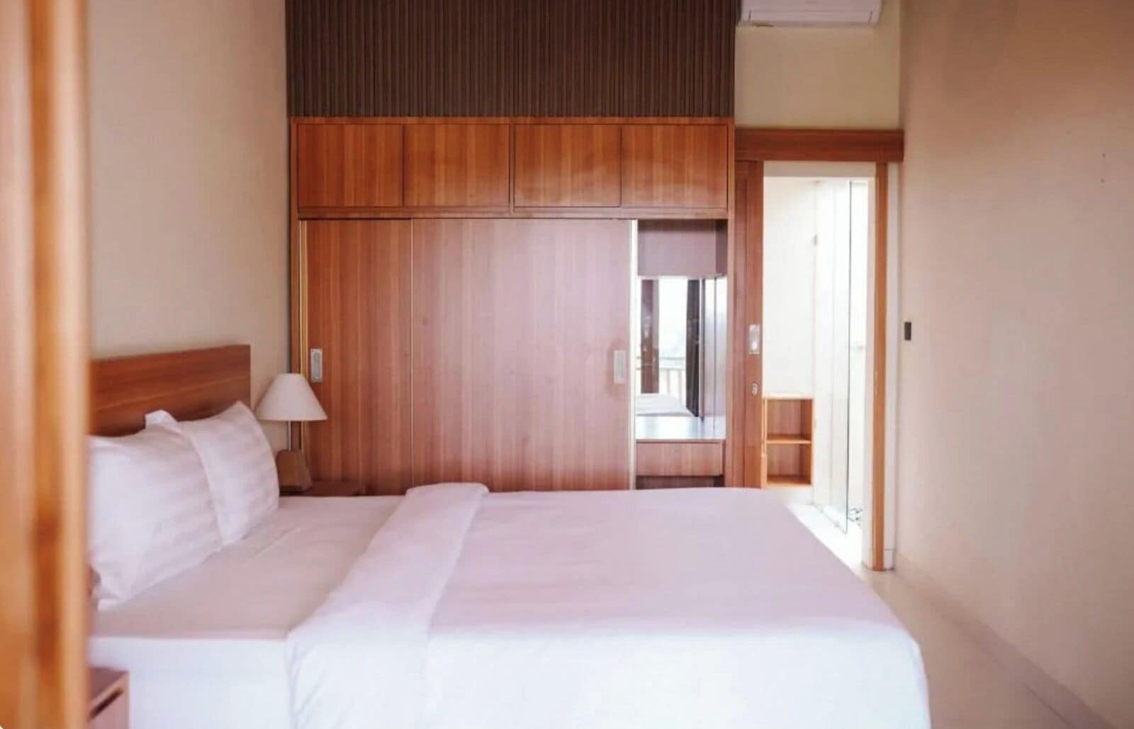 Una habitación de hotel con una cama grande, cabecero de madera y una mesita de noche con lámpara.