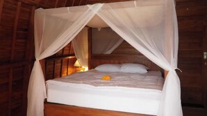 Una cama con dosel blanco y una sola flor amarilla sobre la almohada.