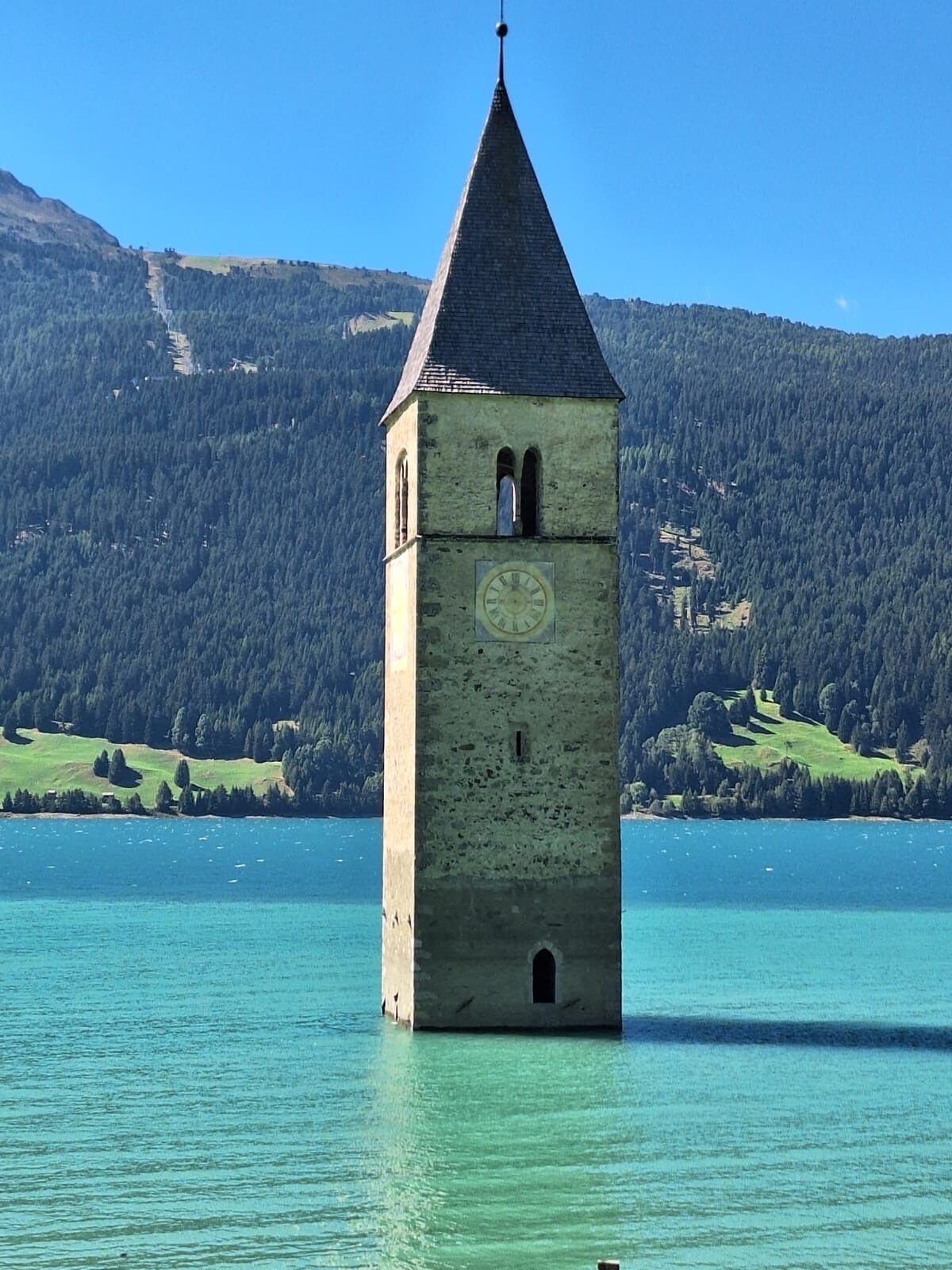 Een toren met een klok, omgeven door een meer en bergen.