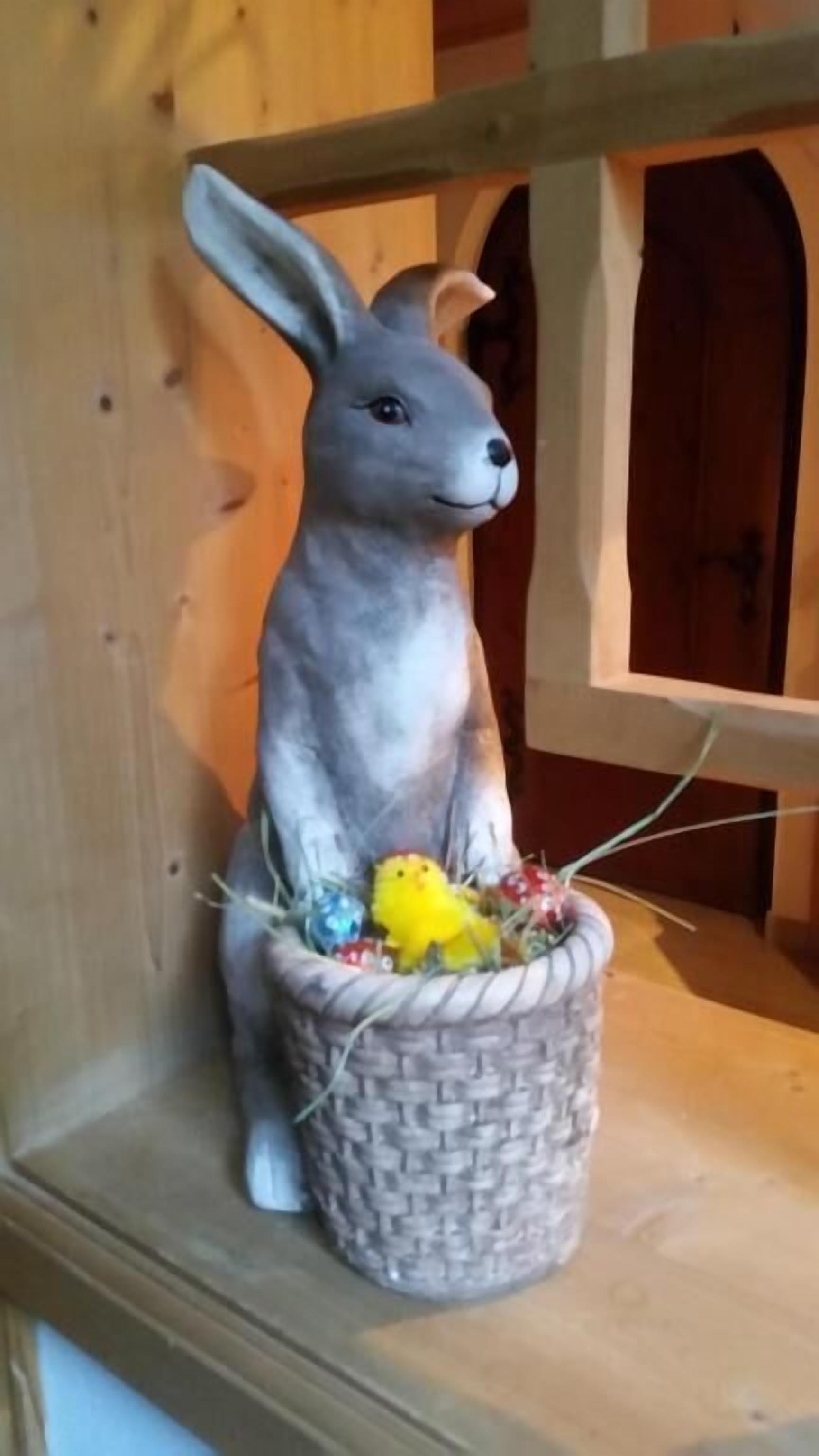 A ceramic rabbit figurine with a basket containing colorful eggs.