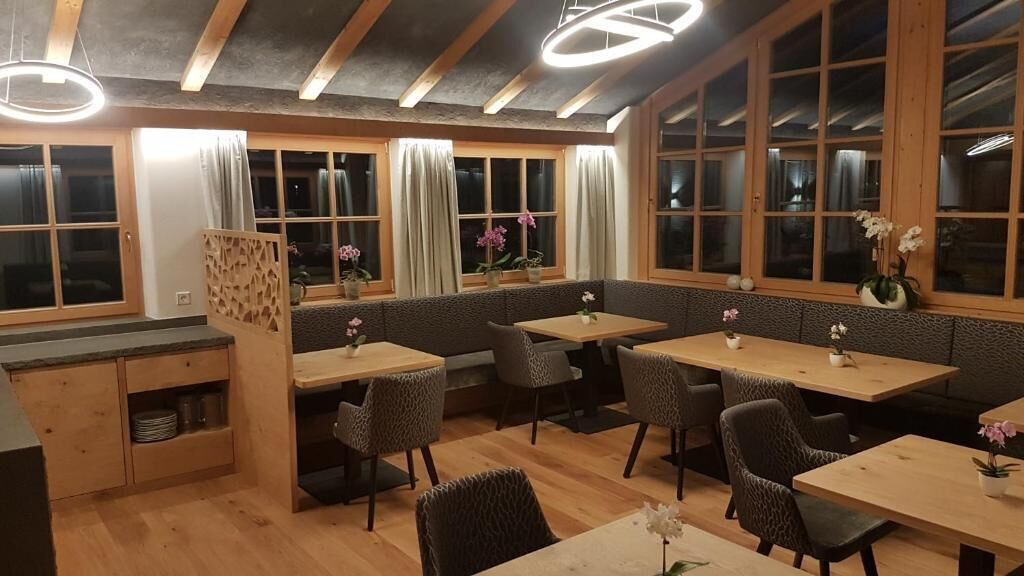 A restaurant with wooden tables and chairs, large windows with curtains, and a modern ceiling design.
