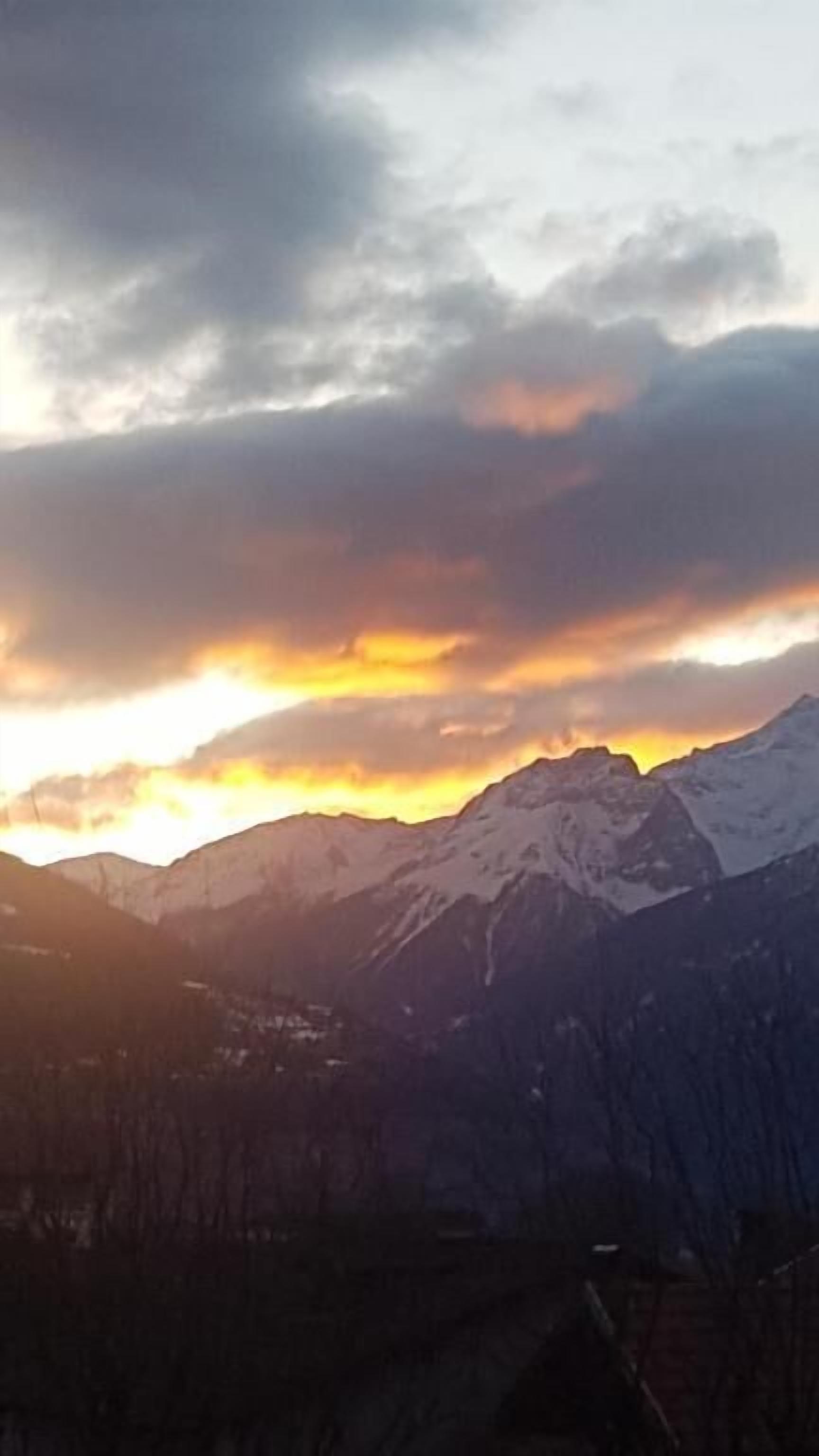 A mountain range with snow-capped peaks and a sunset in the background.