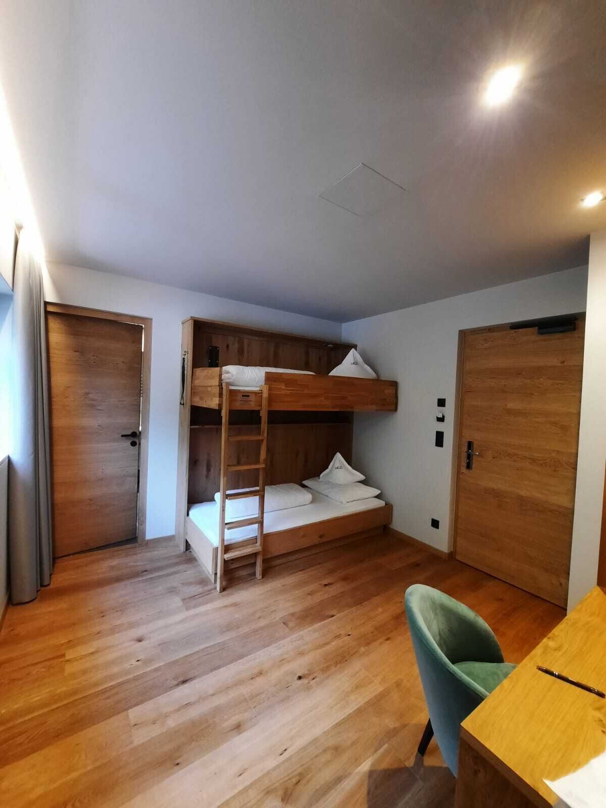 Habitación con literas, un escritorio, una silla, suelo de madera y dos puertas.