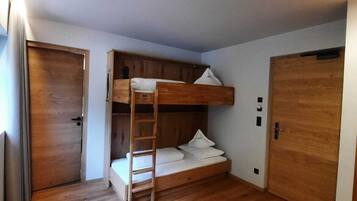 Habitación con literas, un escritorio, una silla, suelo de madera y dos puertas.