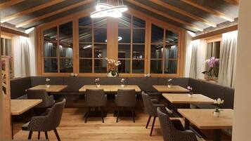 Un restaurante con mesas y sillas de madera, ventanas amplias y un moderno candelabro.